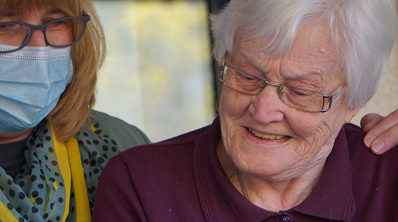 resident and carer who has mask on smiling looking at a phone