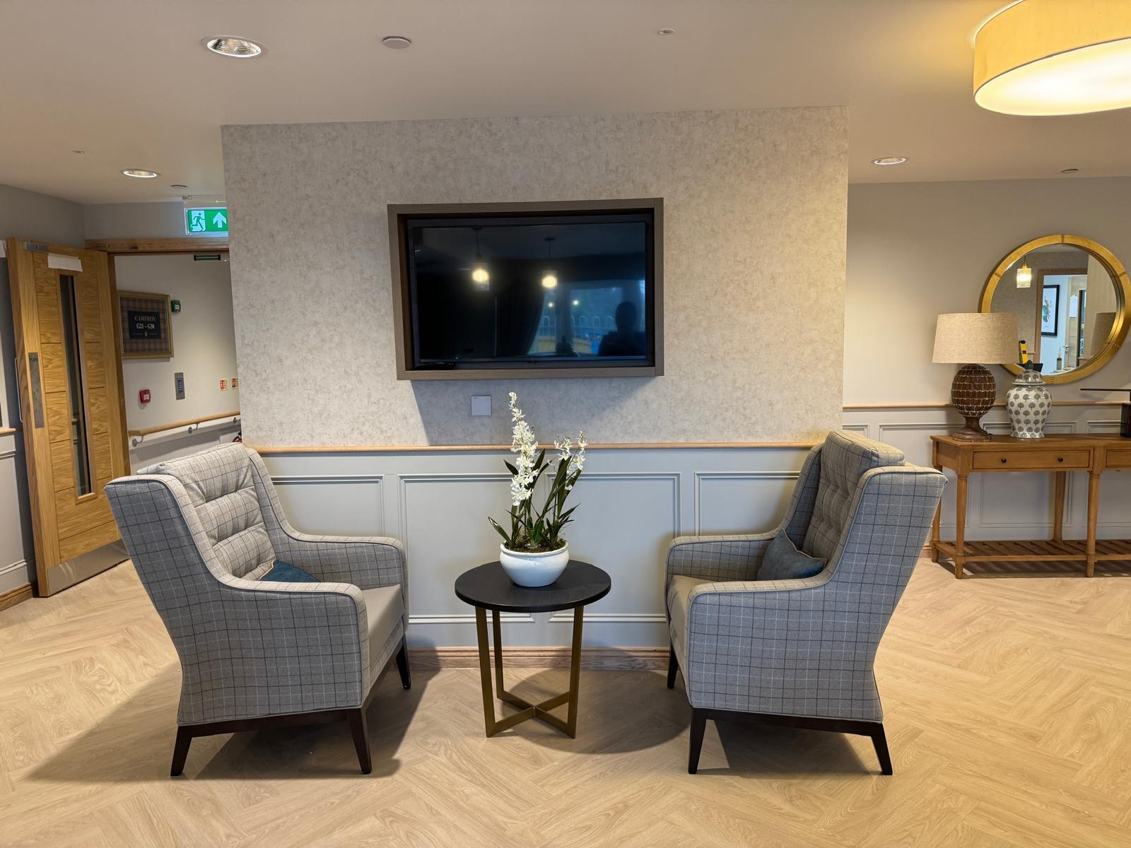 a tv above two grey checkered chairs facing each other in a communal area