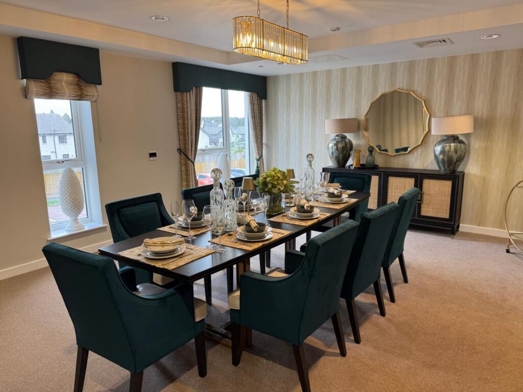 a large dining table and dark green chairs with placemats and cutlery