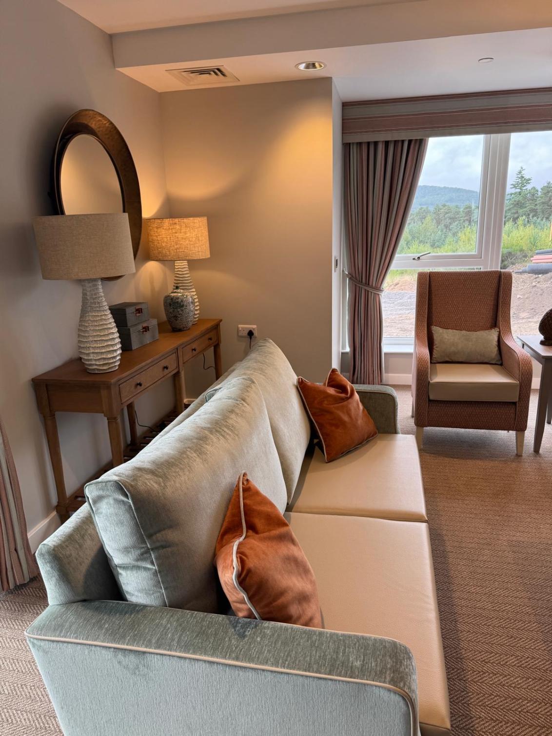 a grey velvet sofa with orange cushions